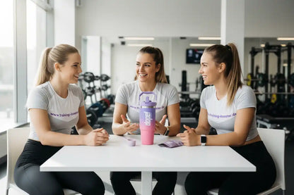 Drei Frauen im Fitnessstudio mit Trainings-Booster-Shirts und Shaker, lächelnd beim Gespräch
