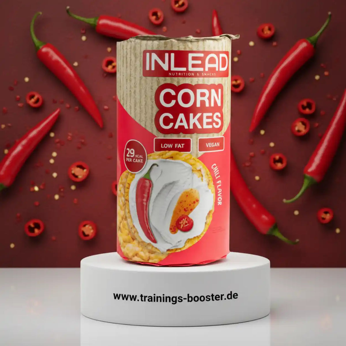 Inlead Nutrition Corn Cakes Verpackung mit Chili-Geschmack auf weißem Podest vor rotem Hintergrund.