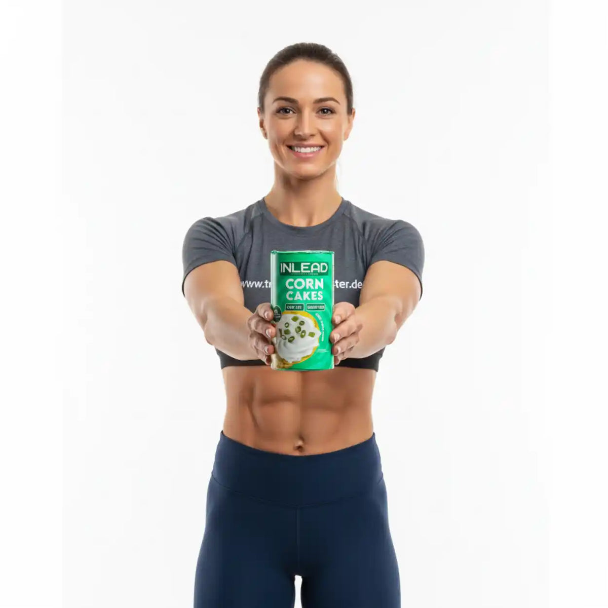 Sportliche Frau hält eine Packung Inlead Nutrition Corn Cakes vor einem weißen Hintergrund.