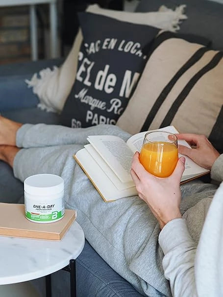 One-A-Day Multivitamin-Dose neben entspannter Person mit Saft und Buch – ideal für tägliche Nahrungsergänzung